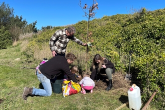 President of Alderney and young child helps Alderney Wildlife Trust CEO and Team Wilder Community Support Officer plant an oak tree within Alderney's Peace Garden