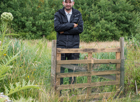 John stands besides a gate on a reserve